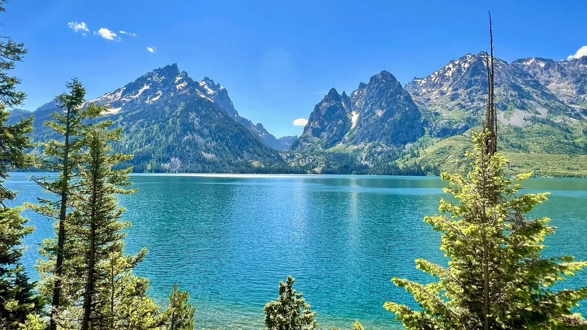 A turquoise mountain lake beneath jagged granite peaks, framed by evergreen trees